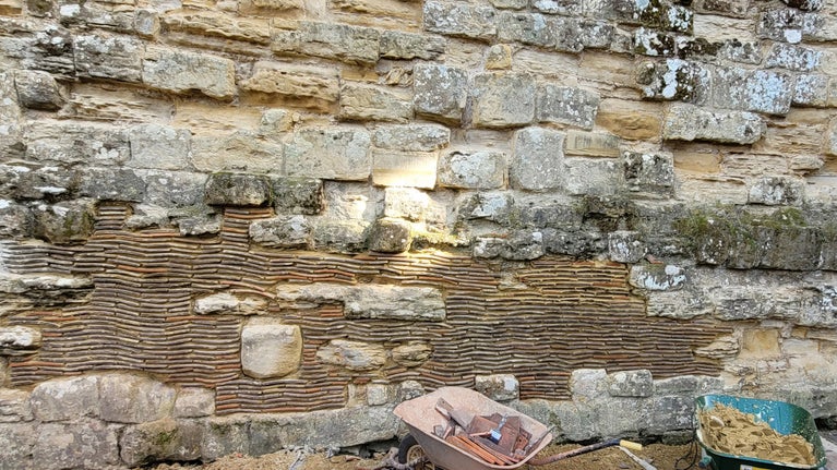 A castle wall repair in progress, showing areas of the sandstone wall infilled with tiles